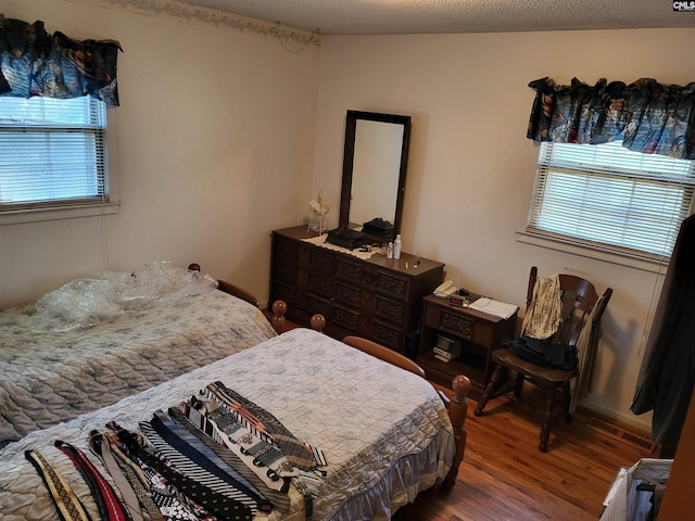 bedroom with a textured ceiling, wood-type flooring, and multiple windows