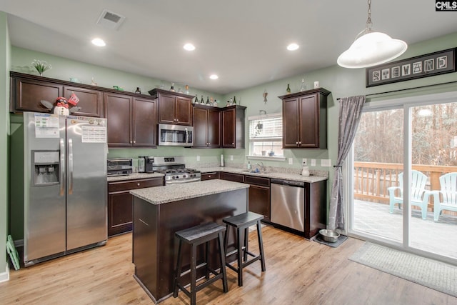 kitchen with a center island, a kitchen bar, light hardwood / wood-style floors, pendant lighting, and appliances with stainless steel finishes