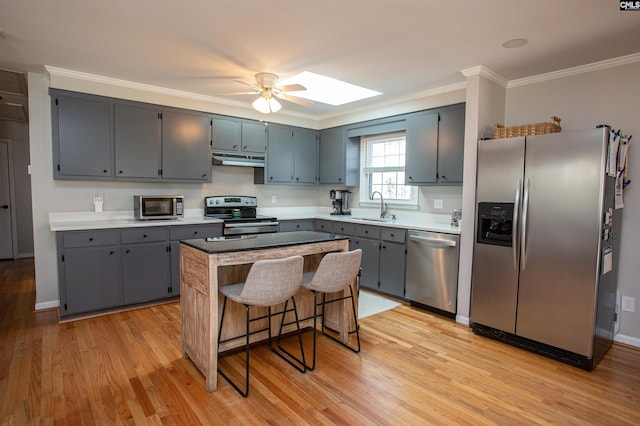 kitchen with stainless steel appliances, a skylight, a center island, crown molding, and sink