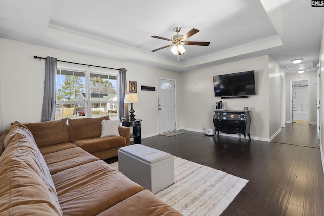 living room featuring a raised ceiling, ceiling fan, ornamental molding, and dark wood-type flooring