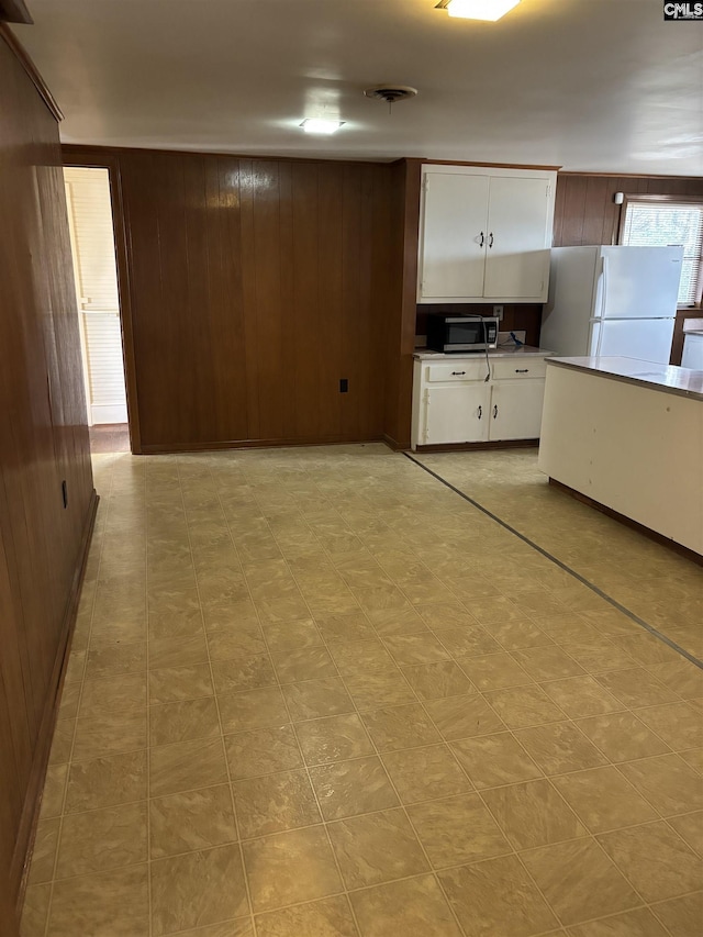 kitchen featuring white fridge, white cabinetry, and wood walls