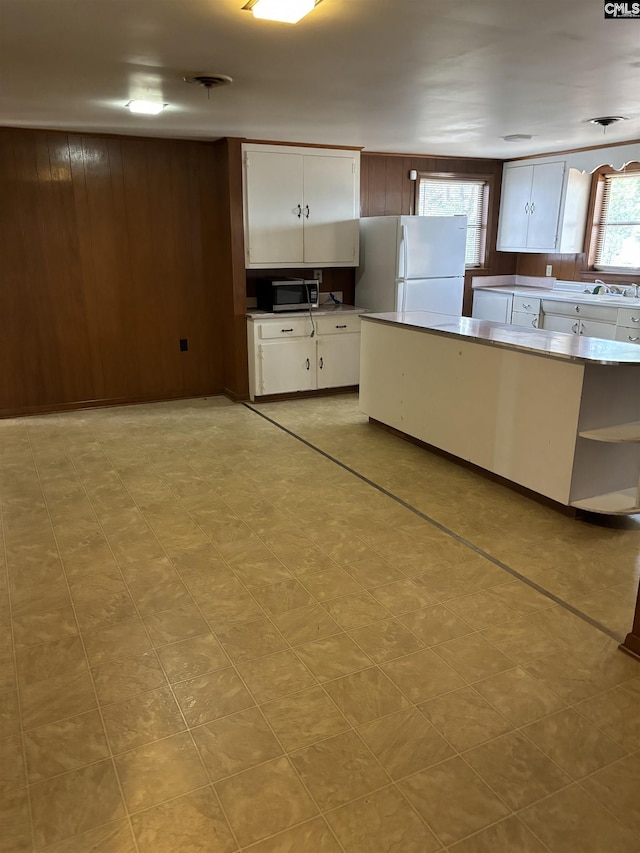 kitchen with sink, white refrigerator, white cabinetry, and wood walls