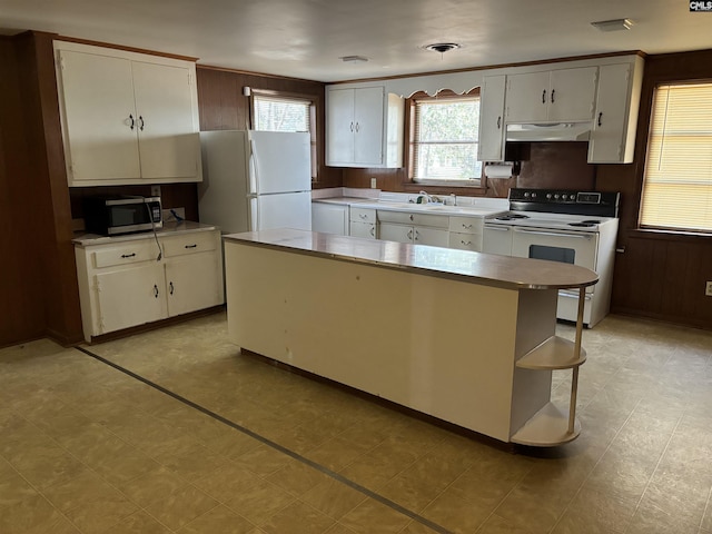 kitchen with white appliances, wooden walls, a kitchen island, white cabinets, and sink