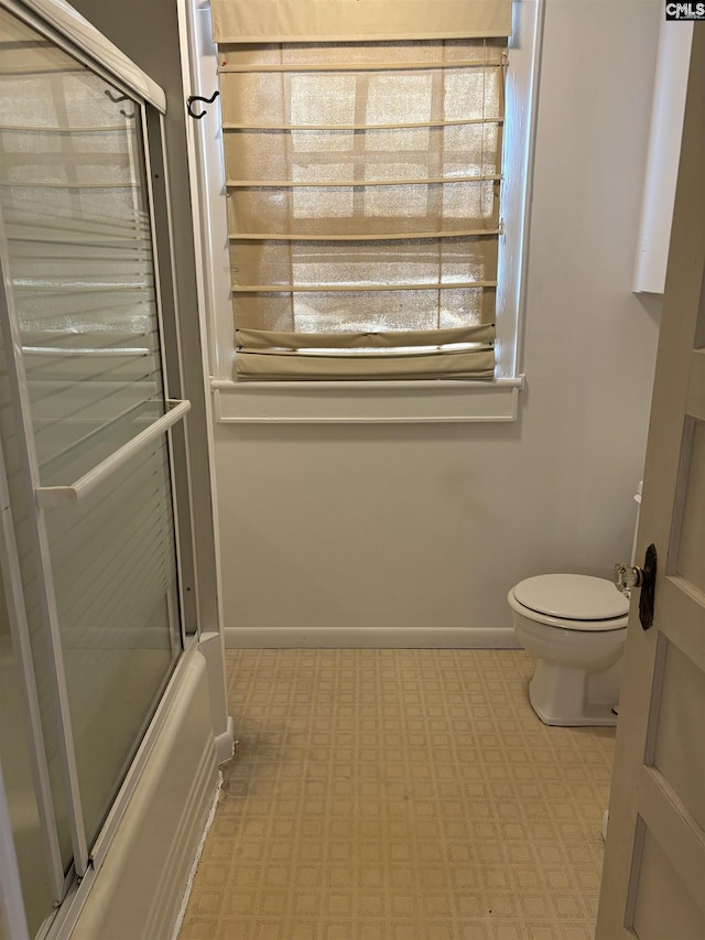 bathroom with toilet and shower / bath combination with glass door