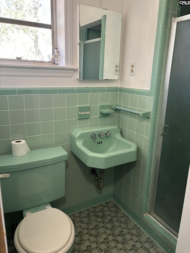 bathroom with tile patterned flooring, toilet, tile walls, a shower with shower door, and sink