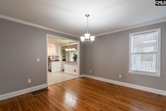 unfurnished dining area featuring an inviting chandelier, ornamental molding, a healthy amount of sunlight, and hardwood / wood-style floors