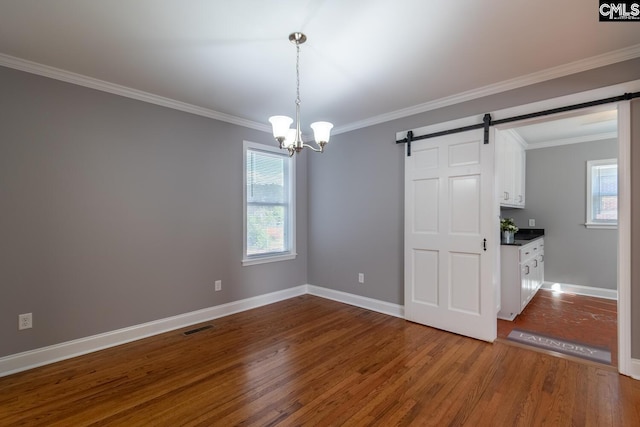 unfurnished dining area with wood-type flooring, a notable chandelier, ornamental molding, and a barn door