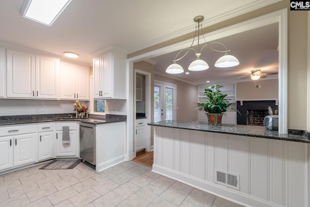 kitchen with dishwasher, crown molding, white cabinetry, a fireplace, and dark stone countertops