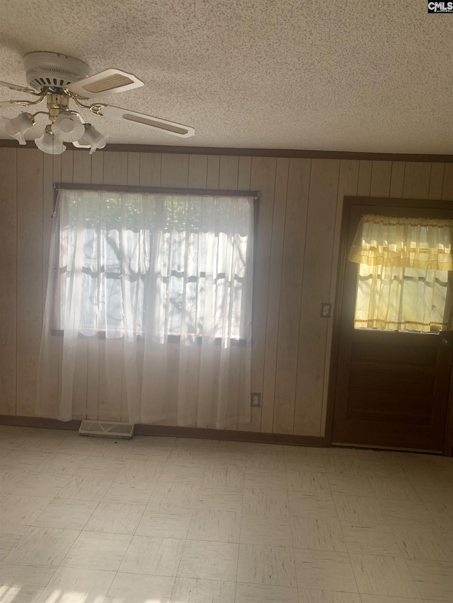 entryway featuring a textured ceiling, wood walls, ceiling fan, and plenty of natural light