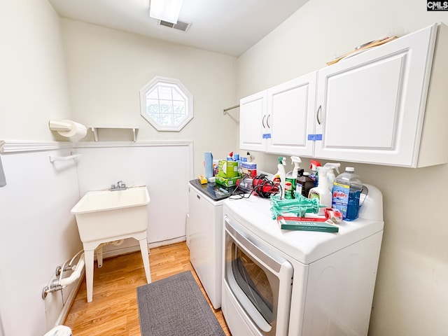 laundry room featuring separate washer and dryer, cabinets, and light hardwood / wood-style flooring