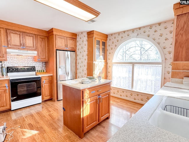 kitchen featuring electric stove, a center island, stainless steel fridge with ice dispenser, light wood-type flooring, and sink