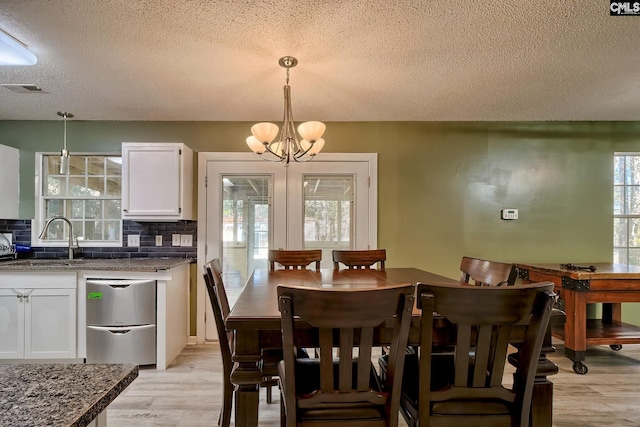 dining space with light wood-type flooring, a textured ceiling, a notable chandelier, and sink