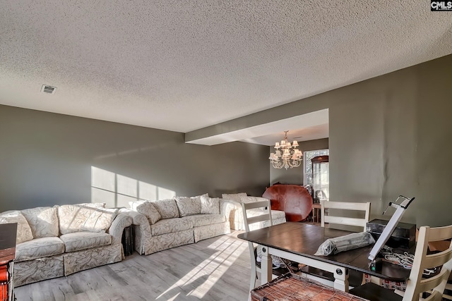 living room with a textured ceiling, a notable chandelier, and light hardwood / wood-style floors