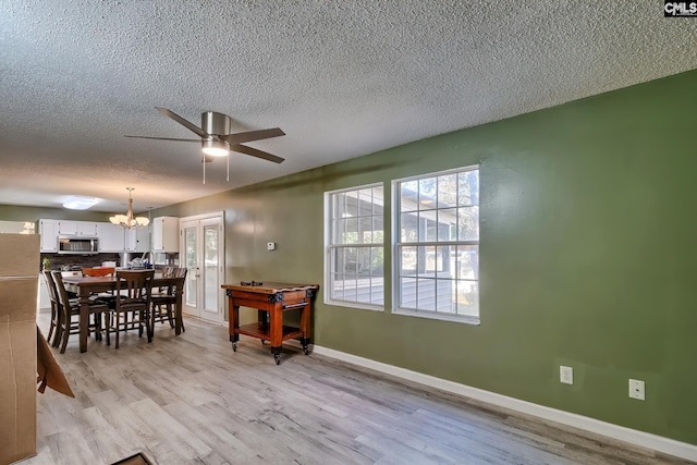 dining space featuring ceiling fan with notable chandelier, french doors, a textured ceiling, and light hardwood / wood-style floors