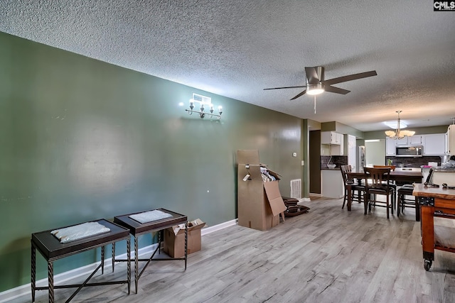 dining area featuring ceiling fan with notable chandelier, a textured ceiling, and light hardwood / wood-style flooring