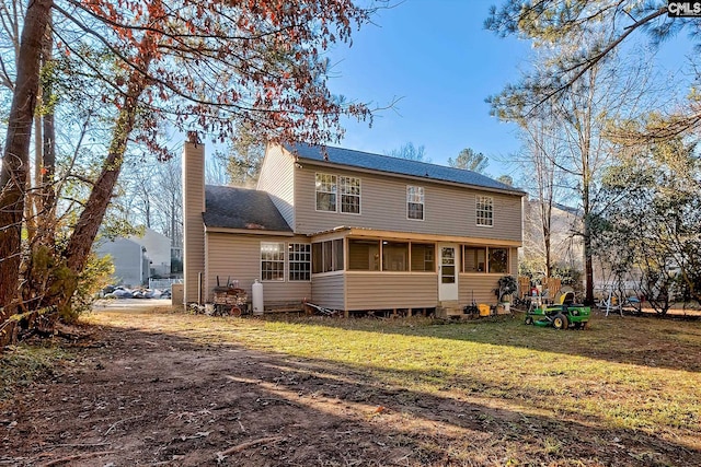 rear view of property with a sunroom, a yard, and a chimney