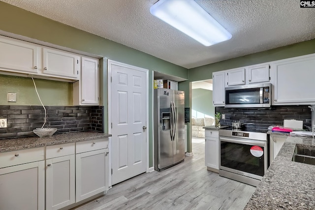 kitchen with light hardwood / wood-style floors, stainless steel appliances, a textured ceiling, white cabinetry, and backsplash