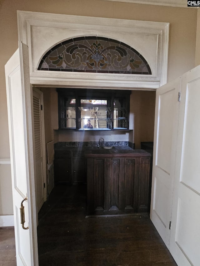 bar featuring sink, dark wood-type flooring, and dark brown cabinets