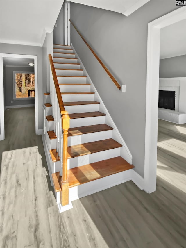 stairway with wood-type flooring, a fireplace, and ornamental molding