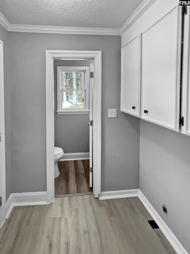 clothes washing area featuring a textured ceiling, ornamental molding, and light hardwood / wood-style flooring