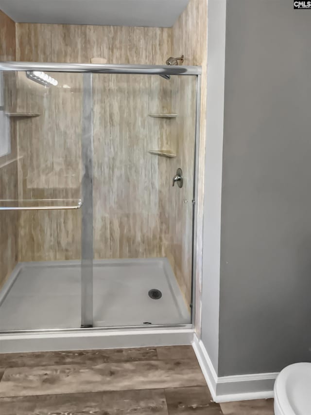 bathroom featuring hardwood / wood-style flooring, a shower with shower door, and toilet