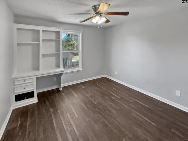 unfurnished office with built in desk, a textured ceiling, ceiling fan, and dark hardwood / wood-style floors