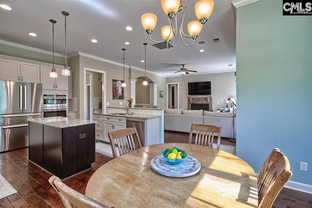 dining room with a stone fireplace, sink, crown molding, dark hardwood / wood-style flooring, and ceiling fan with notable chandelier