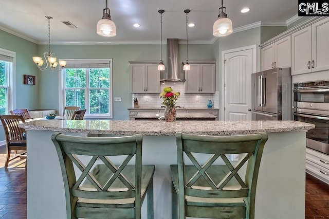 kitchen with appliances with stainless steel finishes, range hood, a breakfast bar area, hanging light fixtures, and a center island with sink