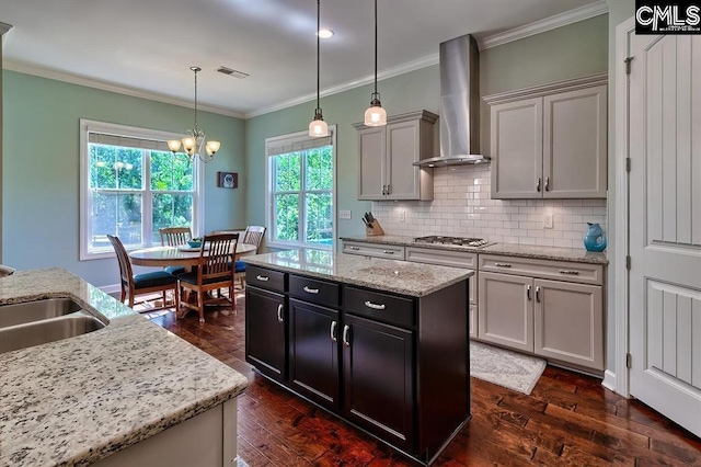 kitchen featuring crown molding, a center island, stainless steel gas cooktop, decorative light fixtures, and wall chimney exhaust hood