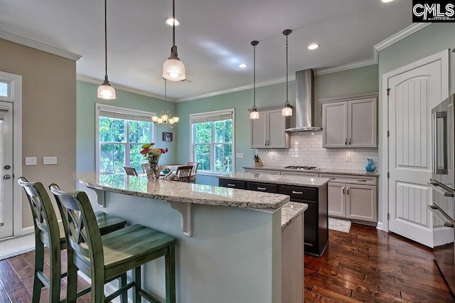 kitchen featuring stainless steel gas stovetop, backsplash, hanging light fixtures, light stone counters, and wall chimney range hood