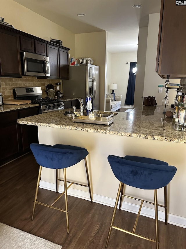 kitchen with kitchen peninsula, dark hardwood / wood-style floors, a kitchen bar, appliances with stainless steel finishes, and dark brown cabinetry