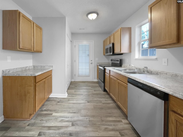 kitchen with a textured ceiling, sink, stainless steel appliances, and light hardwood / wood-style floors