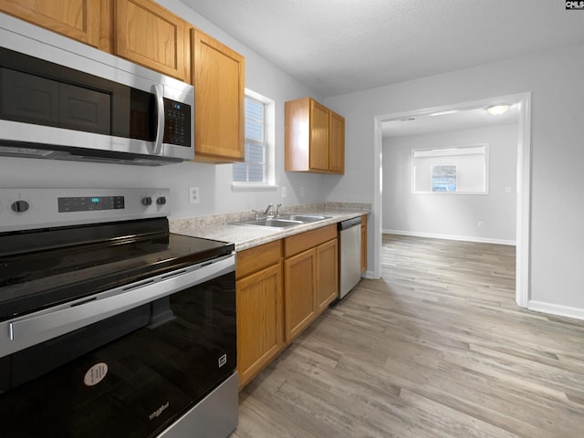 kitchen with a textured ceiling, sink, stainless steel appliances, and light hardwood / wood-style floors