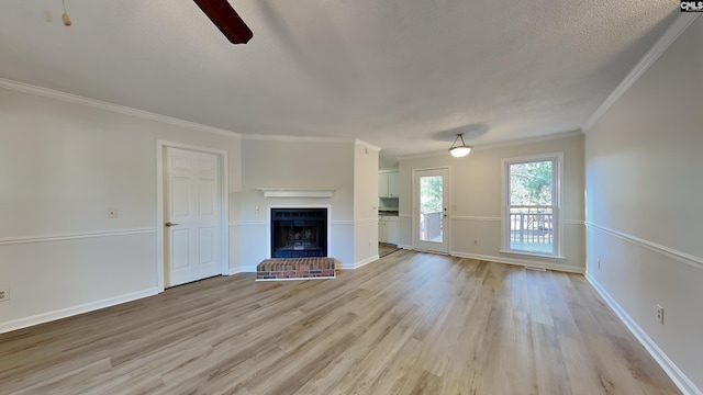 unfurnished living room featuring light hardwood / wood-style floors, crown molding, ceiling fan, a brick fireplace, and a textured ceiling