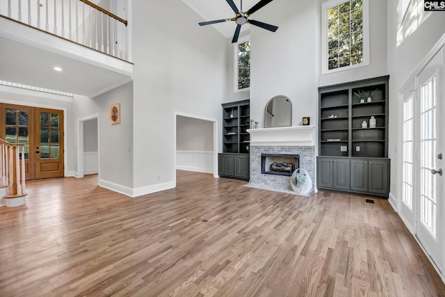 unfurnished living room featuring french doors, a towering ceiling, light wood-type flooring, ceiling fan, and a stone fireplace