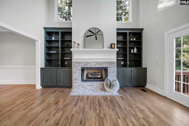 unfurnished living room with light hardwood / wood-style floors, a brick fireplace, and a towering ceiling