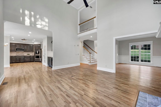 unfurnished living room with a towering ceiling, ceiling fan, light hardwood / wood-style floors, and ornamental molding