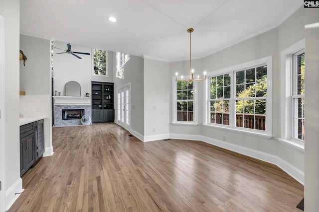 unfurnished living room with ceiling fan with notable chandelier, a fireplace, light wood-type flooring, and ornamental molding