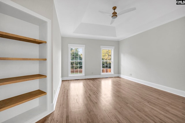 spare room with wood-type flooring, a raised ceiling, ceiling fan, and built in shelves