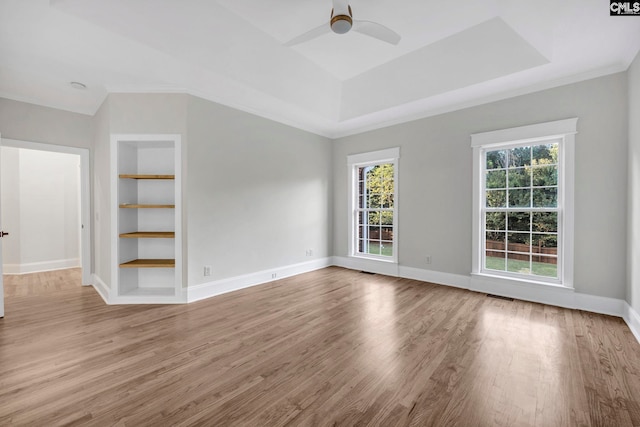 unfurnished room with wood-type flooring, ceiling fan, ornamental molding, a tray ceiling, and built in features