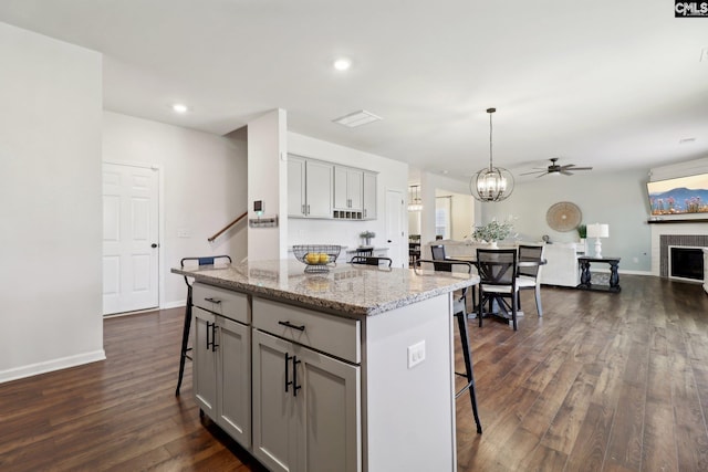 kitchen with gray cabinets, a center island, pendant lighting, a breakfast bar, and light stone counters