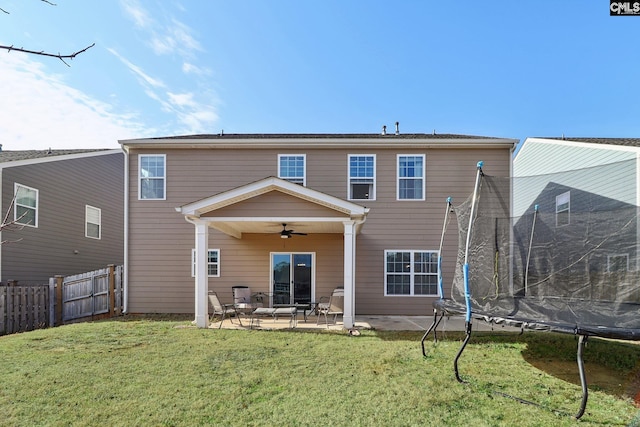 back of house featuring ceiling fan, a patio, fence, a lawn, and a trampoline