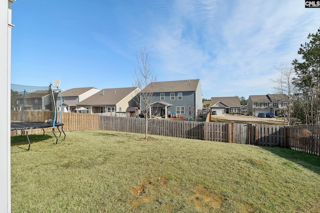 view of yard featuring a trampoline, a fenced backyard, and a residential view