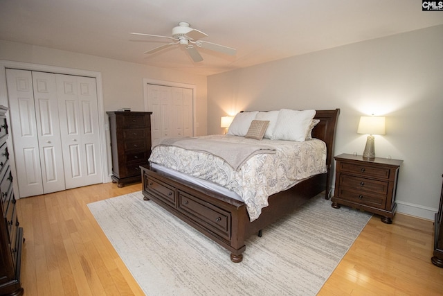 bedroom with ceiling fan, light wood-type flooring, and two closets