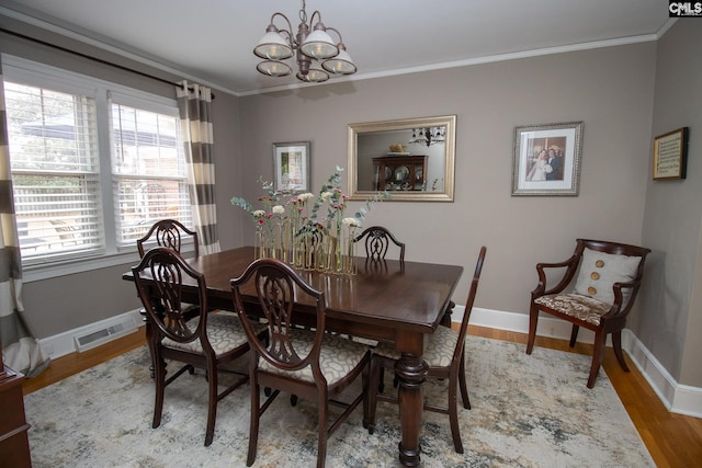 dining area with light wood-type flooring, an inviting chandelier, and crown molding