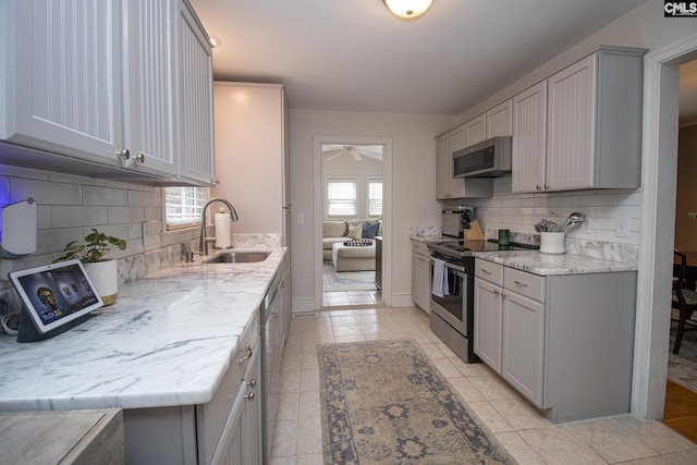 kitchen featuring sink, ceiling fan, backsplash, light stone countertops, and appliances with stainless steel finishes