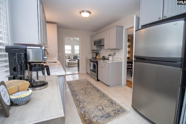 kitchen with stainless steel appliances, decorative backsplash, light tile patterned floors, and gray cabinets