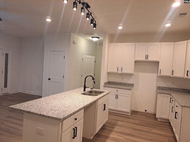 kitchen featuring sink, hardwood / wood-style flooring, white cabinetry, light stone countertops, and an island with sink