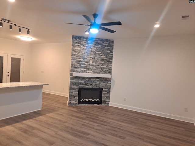 unfurnished living room with rail lighting, ceiling fan, dark wood-type flooring, french doors, and a fireplace