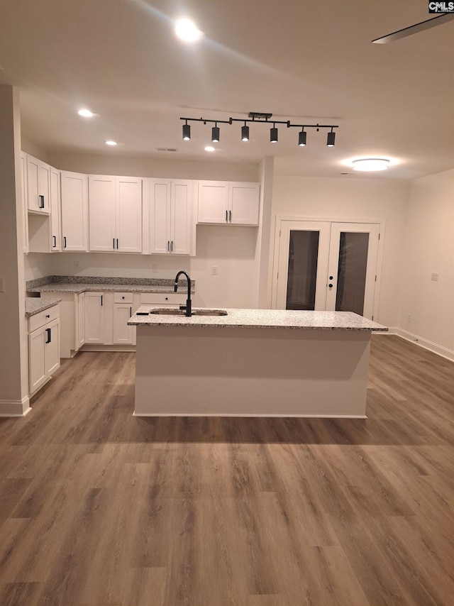 kitchen featuring white cabinetry, sink, wood-type flooring, and a center island with sink